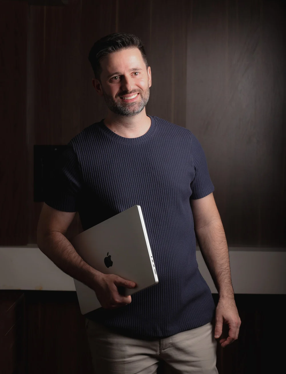 Danilo Orsi sorrindo, em pé e segurando um notebook
